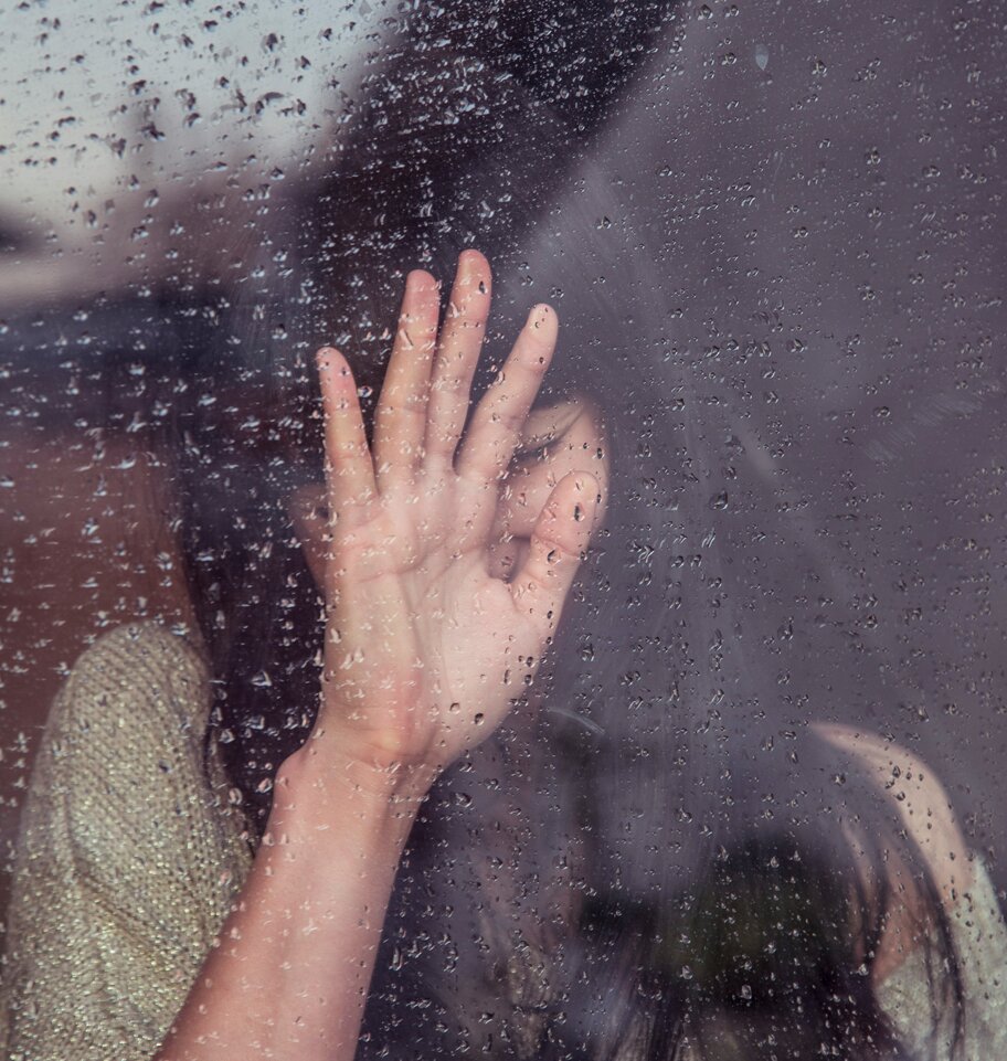 Grieving woman resting against a rain-covered window