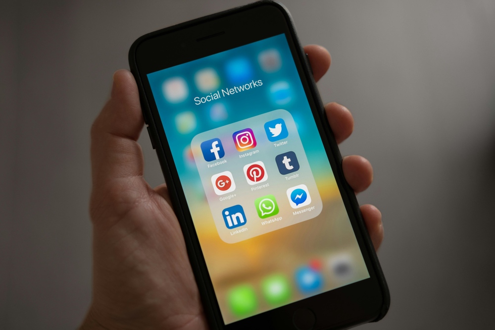 Hand holding iphone with social media icons on screen